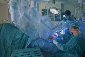 A imagem é uma cirurgia robótica na coluna, possui médicos vestido de azul operando uma pessoa com auxílio de robôs.